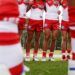 A pair of blurry legs in the foreground with a line of Sydney Swans players in the background