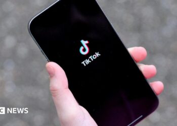 A young woman holding her iPhone while showing the TikTok app.