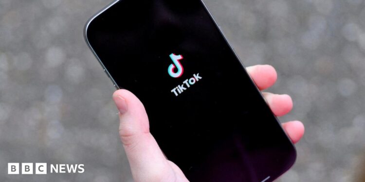 A young woman holding her iPhone while showing the TikTok app.