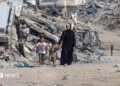 A Palestinian woman walks with children along a path lined with piles of rubble in the Sheikh Radwan neighbourhood of Gaza City