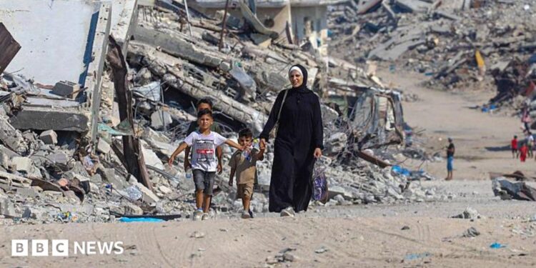 A Palestinian woman walks with children along a path lined with piles of rubble in the Sheikh Radwan neighbourhood of Gaza City