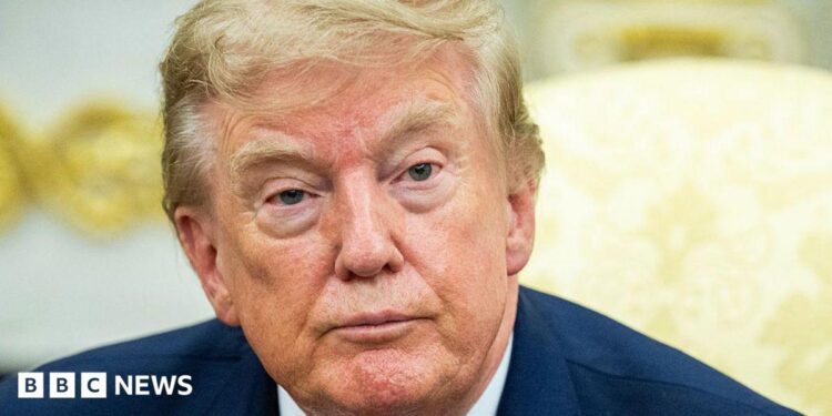 Donald Trump in a navy suit with a yellow background.