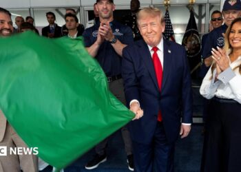 Donald Trump waves a green flag as he stands next to his wife Melania who is smiling and clapping