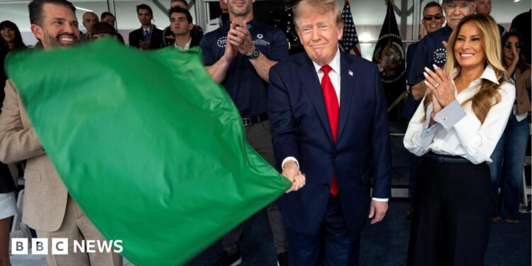 Donald Trump waves a green flag as he stands next to his wife Melania who is smiling and clapping