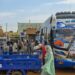 A coach is parked on the right-hand side of the picture. A group of people are standing close by gathering luggage. In the foreground, an open-backed tuktuk is parked.