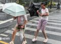 People holding umbrellas along a street in Shanghai. One boy is seen trying to hold on to an inverted umbrella as winds intensify