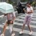 People holding umbrellas along a street in Shanghai. One boy is seen trying to hold on to an inverted umbrella as winds intensify