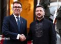 Burnham and Zelensky pose looking at the camera while shaking hands with soldiers behind them, on the steps of Horodetskyi House in Kyiv on Monday.