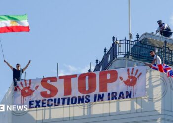 Protesters hold a banner saying "stop executions in Iran" and wave an Iranian flag during a demonstration on the roof of the Trocadero, overlooking Piccadilly Circus, central London (30 July 2026)