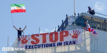 Protesters hold a banner saying "stop executions in Iran" and wave an Iranian flag during a demonstration on the roof of the Trocadero, overlooking Piccadilly Circus, central London (30 July 2026)