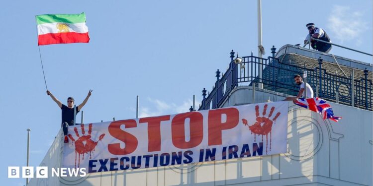 Protesters hold a banner saying "stop executions in Iran" and wave an Iranian flag during a demonstration on the roof of the Trocadero, overlooking Piccadilly Circus, central London (30 July 2026)