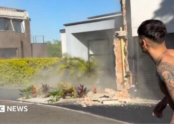 A topless man stands in the street while an earthquake damages buildings around him