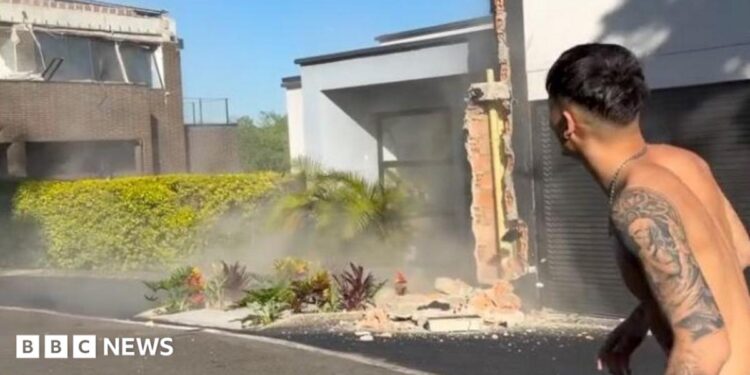 A topless man stands in the street while an earthquake damages buildings around him