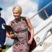 Natalie Harp walks off Air Force One wearing a sleeveless printed red dress. She is smiling and has a laptop in her hands.