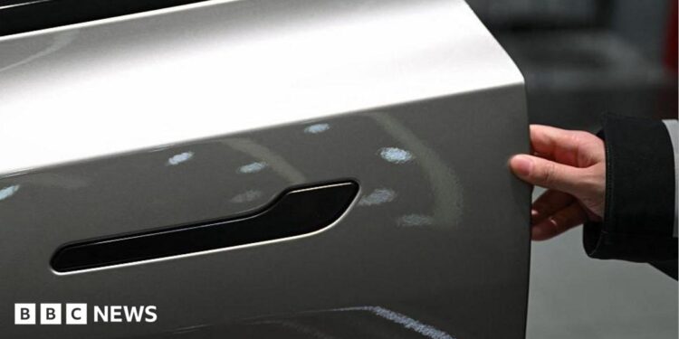 A customer inspects the minimalistic hidden door handles on an electric car in a showroom.