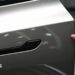 A customer inspects the minimalistic hidden door handles on an electric car in a showroom.