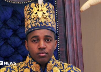 King Oyo pictured at 18 during his coronation wearing a gold embroidered jacket and hat.