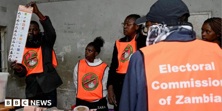 An election official displays a ballot paper as observers look on during the counting of votes after the polls closed at a polling station in Lusaka, Zambia