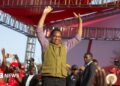 Zambia's President Hakainde Hichilema in green half-coat and black trousers lifts his hands to greet United Party for National Development supporters