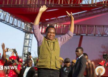 Zambia's President Hakainde Hichilema in green half-coat and black trousers lifts his hands to greet United Party for National Development supporters