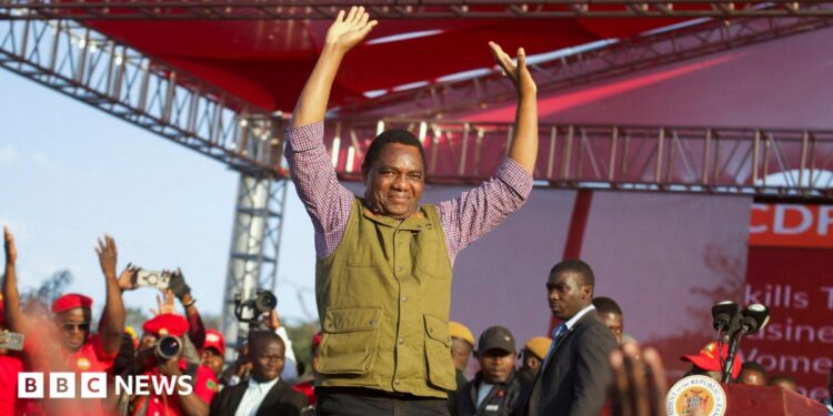 Zambia's President Hakainde Hichilema in green half-coat and black trousers lifts his hands to greet United Party for National Development supporters