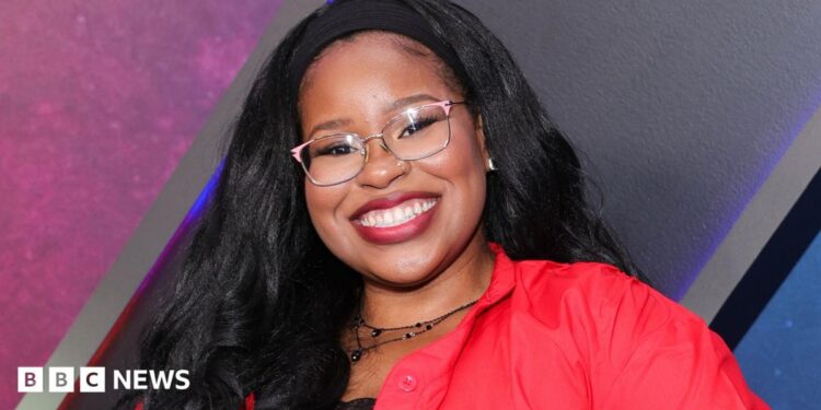 Carla Jeffery grinning in glasses and a red blouse, posing for photos at the world premiere of Disney's Zombies 4: Dawn Of The Vampires at El Capitan Theatre on 8 July, 2025 in Los Angeles.