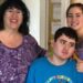Linda Mancuso, wearing a purple top, glasses and dark hair falling to her shoulders, stands next to her 23-year-old son, Michael, who needs 24/7 care; he wears a "Happy Birthday" blue shirt and stares off to the side; her daughter stands to the other side of Michael, smiling as she rests a hand on his shoulder