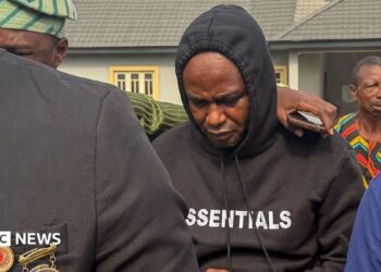 Adeniyi Mobolaji Kayode is in a black hoody with his head bowed as someone has their arm round him as he is led from court in a picture taken in January 20 this year