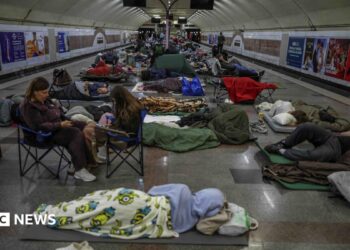 People sleeping on camping mats and sitting in fold out chairs inside a metro station during a Russian strike in Kyiv.