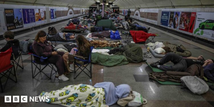 People sleeping on camping mats and sitting in fold out chairs inside a metro station during a Russian strike in Kyiv.