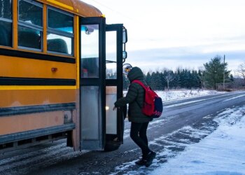 A teen boarding a school bus on a snowy country road.