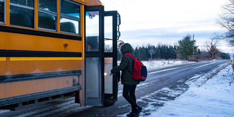 A teen boarding a school bus on a snowy country road.