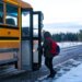 A teen boarding a school bus on a snowy country road.