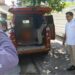 A person stands inside the rear end of an orange van while several other people stand beside the vehicle