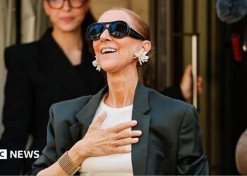Celine Dion with a hand over her chest coming out of her hotel.