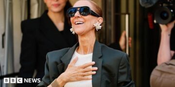 Celine Dion with a hand over her chest coming out of her hotel.