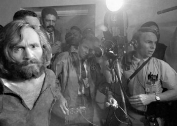 Charles Manson handcuffed being escorted to jail as the press photographs him.