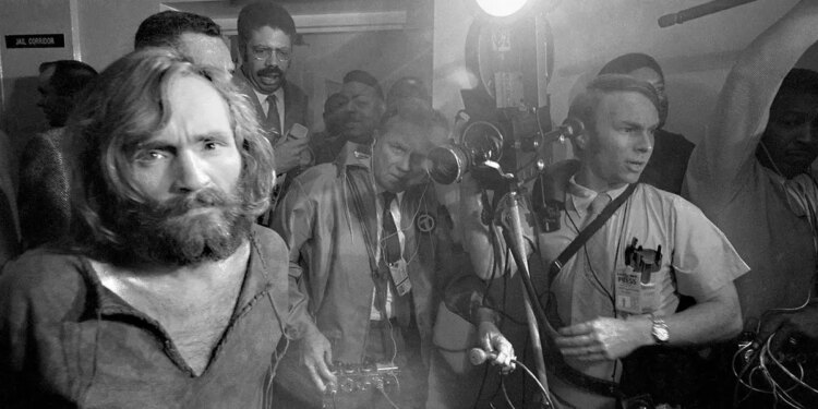 Charles Manson handcuffed being escorted to jail as the press photographs him.