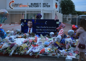 A woman in a pink dress approaches a makeshift memorial for Charlie Kirk outside a Turning Point USA office in Arizona at dusk