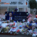 A woman in a pink dress approaches a makeshift memorial for Charlie Kirk outside a Turning Point USA office in Arizona at dusk