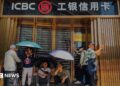 People sit and rest in front of a closed ICBC credit card service centre, shielding themselves from the sun with umbrellas, on 19 April, 2025 in Chongqing, China.