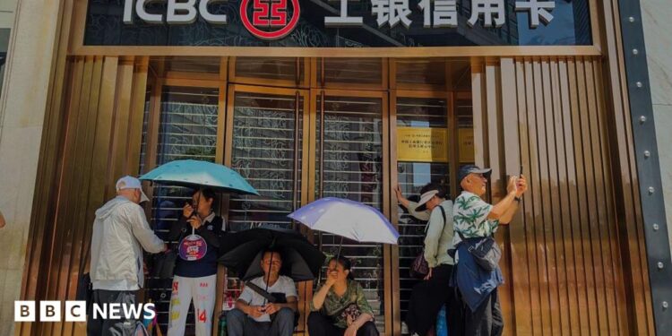 People sit and rest in front of a closed ICBC credit card service centre, shielding themselves from the sun with umbrellas, on 19 April, 2025 in Chongqing, China.