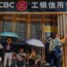 People sit and rest in front of a closed ICBC credit card service centre, shielding themselves from the sun with umbrellas, on 19 April, 2025 in Chongqing, China.