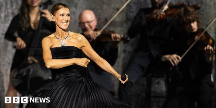 Dion dancing in a black dress, holding a microphone, while musicians play behind her
