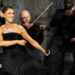 Dion dancing in a black dress, holding a microphone, while musicians play behind her
