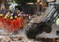 National Disaster Response Force (NDRF) personnel look on at a building collapse in Delhi, while a crushed car is pulled by a digger from the rubble.