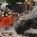 National Disaster Response Force (NDRF) personnel look on at a building collapse in Delhi, while a crushed car is pulled by a digger from the rubble.