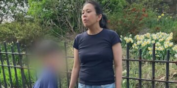 Antoinette Forbes stands outdoors next to her young son, whose face is blurred, in a family photo.