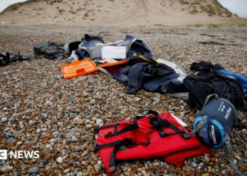 A red life jacket, bags, and other belongings left abandoned on a stony beach, following the death of at least 30 migrants on the English channel in November 2021
