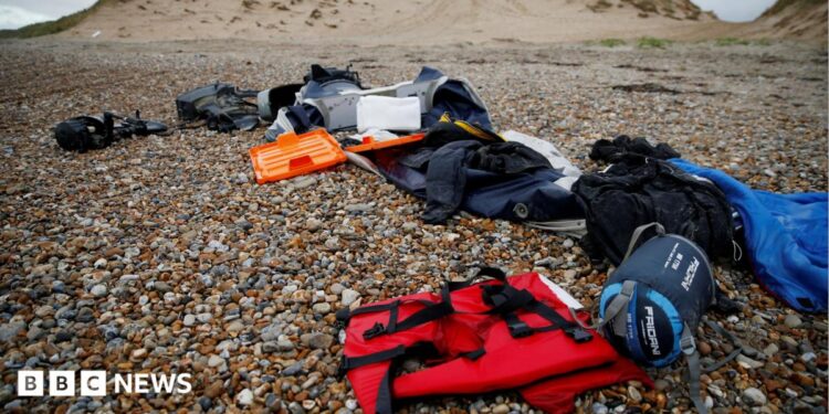 A red life jacket, bags, and other belongings left abandoned on a stony beach, following the death of at least 30 migrants on the English channel in November 2021